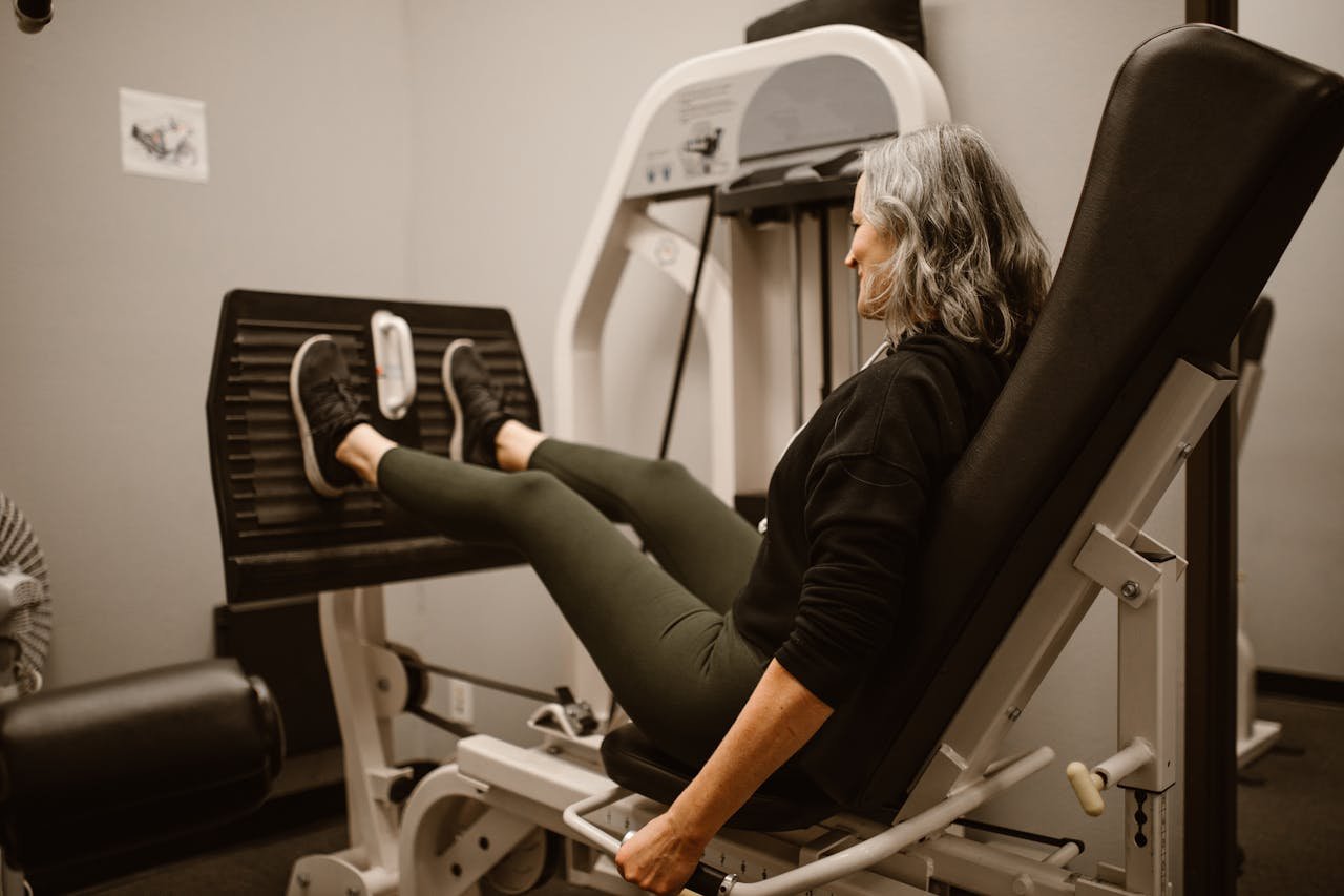 Mature woman working out on a leg press machine in a gym, promoting active and healthy lifestyle.